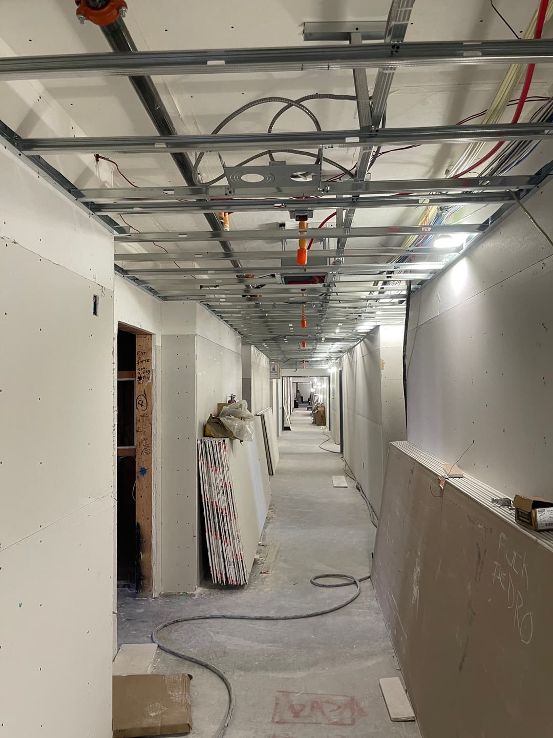 Construction corridor featuring drywall, plumbing, and electrical work in progress.