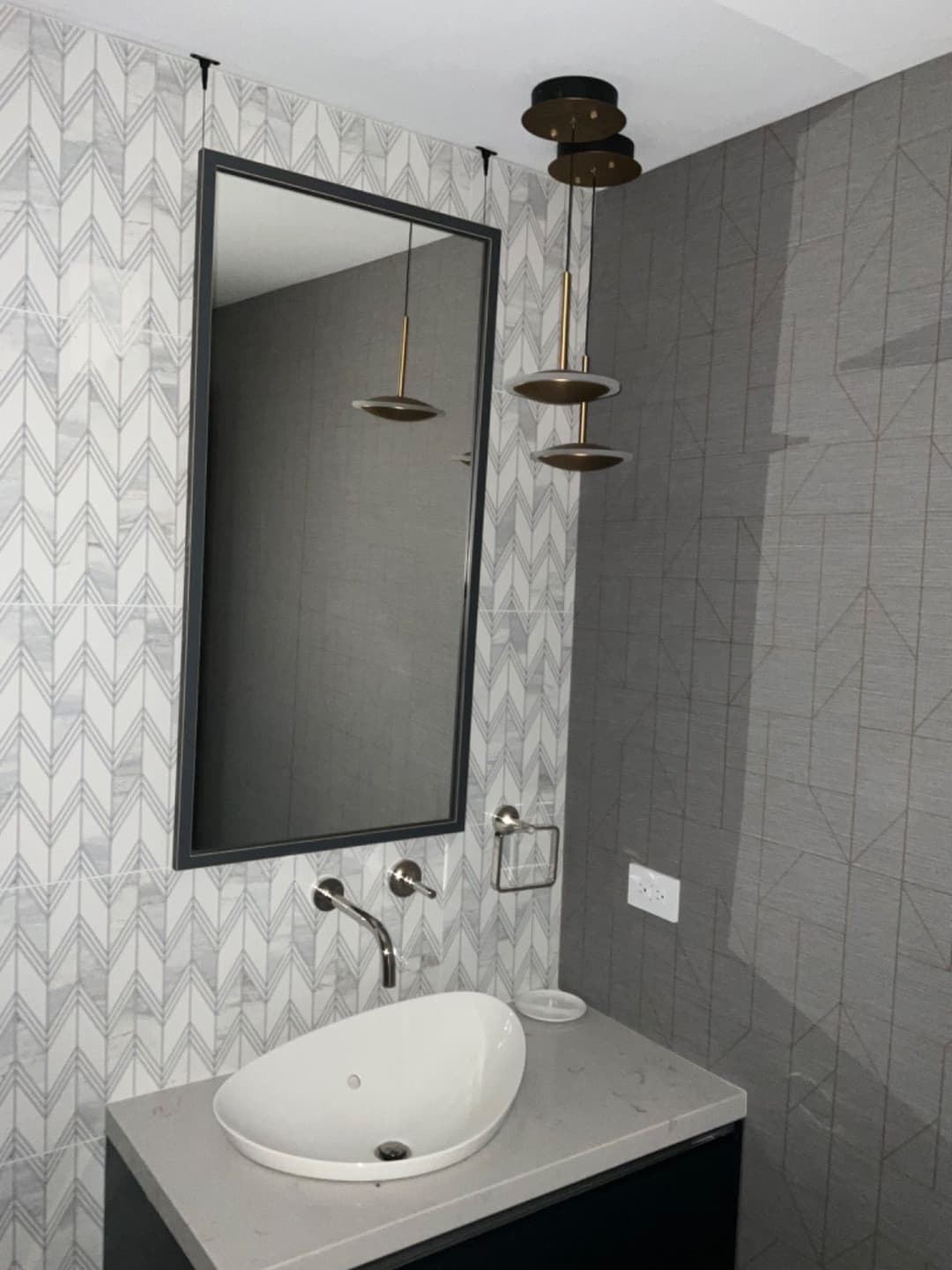 Modern bathroom featuring a geometric wallpaper, elegant mirror, and stylish pendant lights.