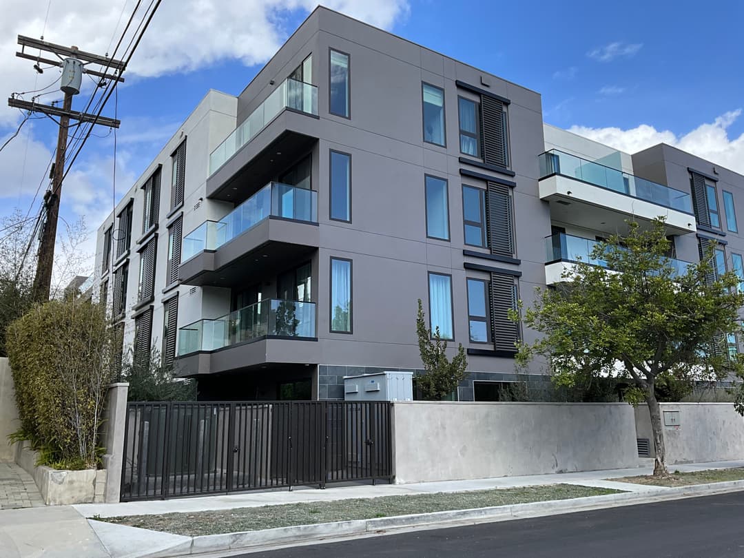 Modern apartment building with balconies, glass railings, and landscaped entrance.