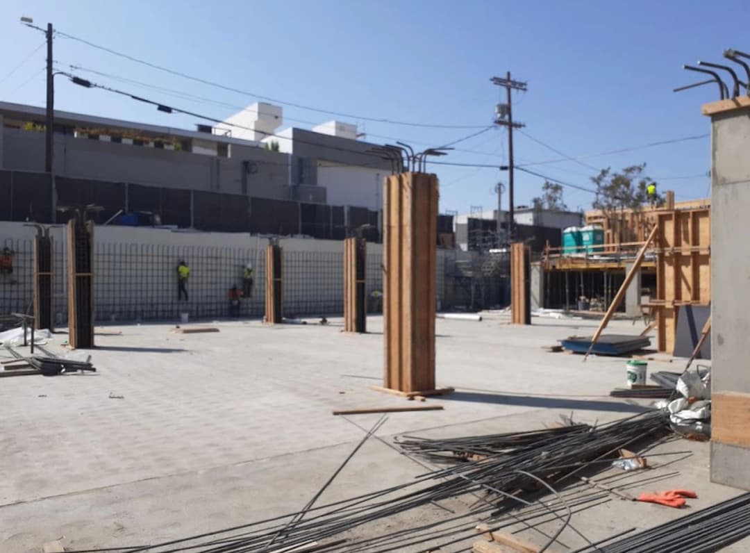 Construction site with concrete pillars, rebar, and workers in safety gear. Clear blue sky.