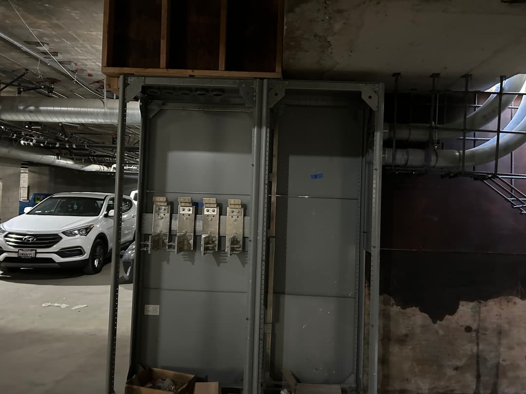 Utility room with electrical panels, storage boxes, and a parked SUV in the background.