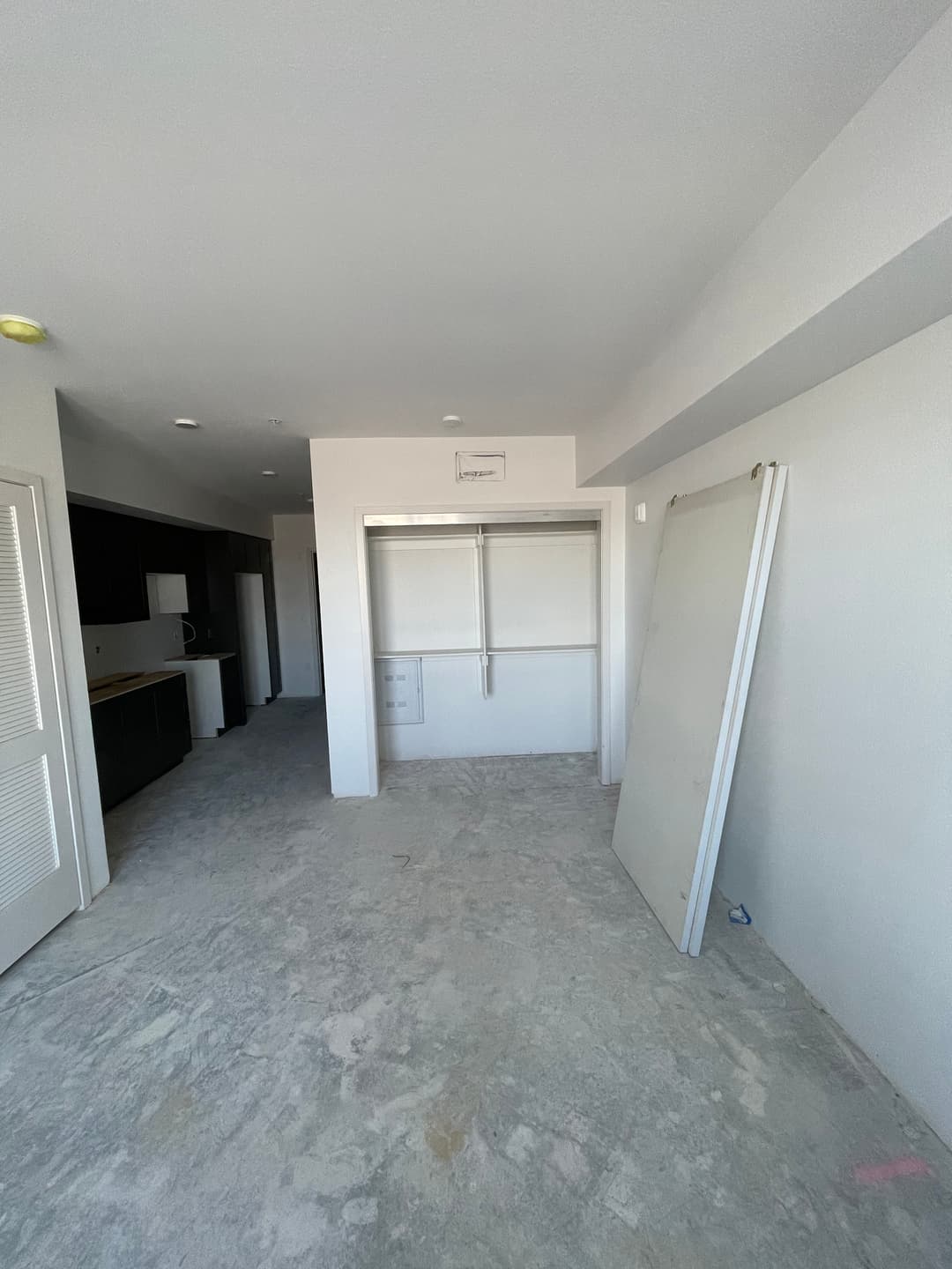 Empty room with unfinished flooring, sliding door, and drywall leaning against the wall.